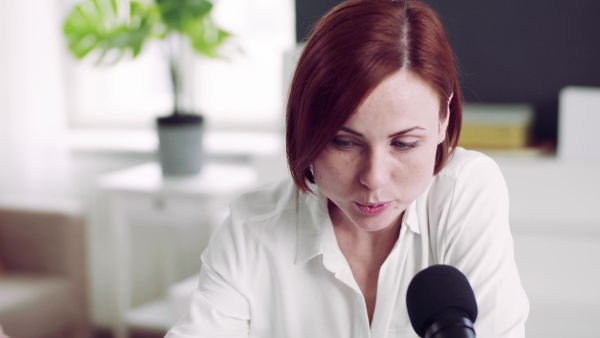 A front view of young woman indoors, recording a podcast at home.