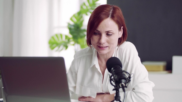 A front view of young woman indoors, recording a podcast at home.