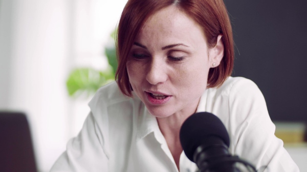 A front view of young woman indoors, recording a podcast at home.