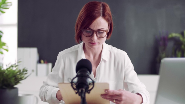 A front view of young woman indoors, recording a podcast at home.