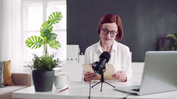 A front view of young woman indoors, recording a podcast at home.