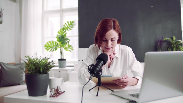 A front view of young woman indoors, recording a podcast at home.