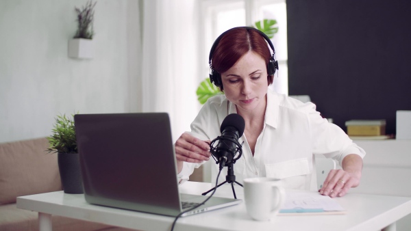 A front view of young woman indoors, recording a podcast at home.