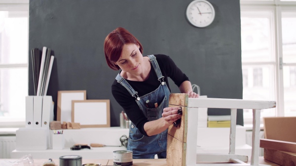 Young woman standing indoors restoring old furniture.