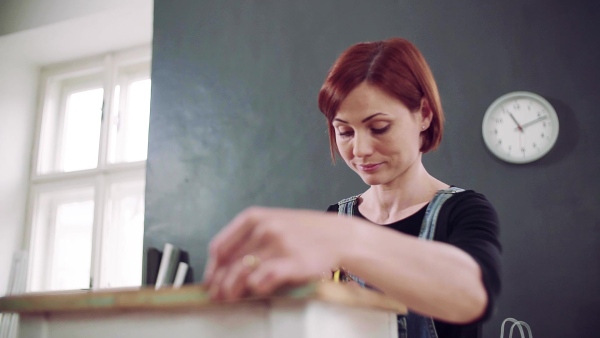 Young woman standing indoors restoring old furniture. Slow motion.