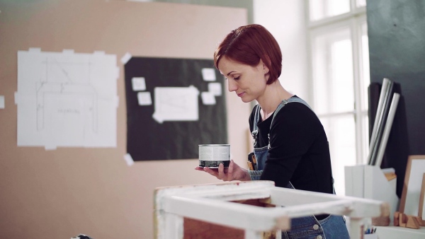 Young woman standing indoors restoring old furniture. Slow motion.