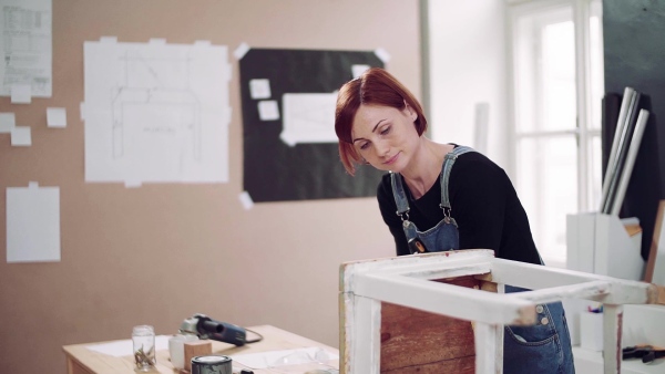 Young woman standing indoors restoring old furniture. Slow motion.