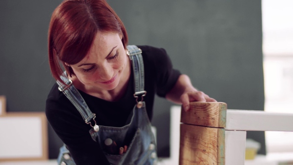 Young woman standing indoors restoring old furniture.