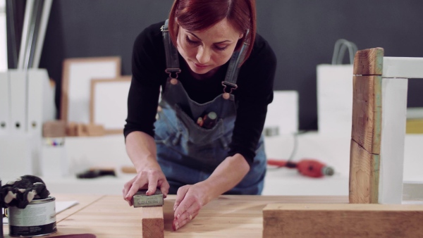 Young woman standing indoors restoring old furniture.