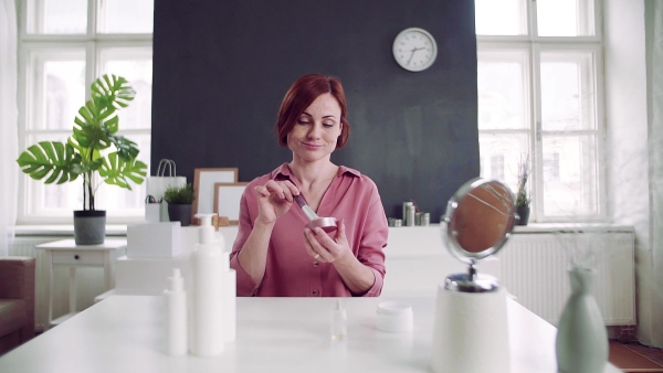 Front view of young woman vlogger showing how to apply makeup indoors, video about beauty products. Slow motion.