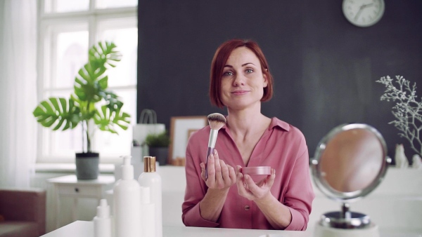 Front view of young woman vlogger showing how to apply makeup indoors, video about beauty products. Slow motion.