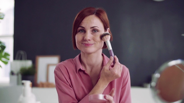 Front view of young woman vlogger showing how to apply makeup indoors, video about beauty products. Slow motion.