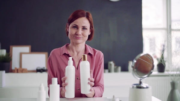 A front view of young woman vlogger indoors, making video about beauty products. Slow motion.