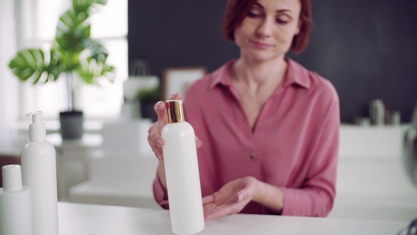 A front view of young woman vlogger indoors, making video about beauty products. Slow motion.