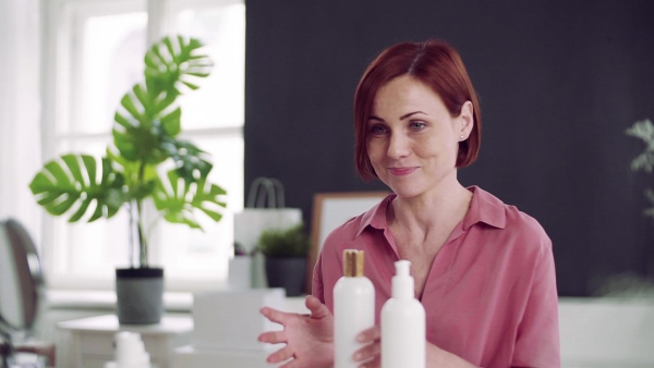 A front view of young woman vlogger indoors, making video about beauty products. Slow motion.