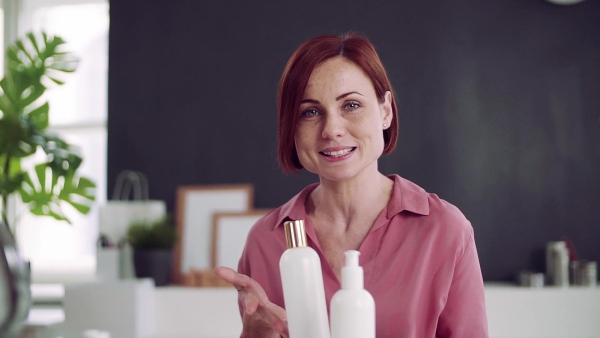 A front view of young woman vlogger indoors, making video about beauty products. Slow motion.