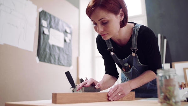 Young woman standing indoors restoring old furniture.