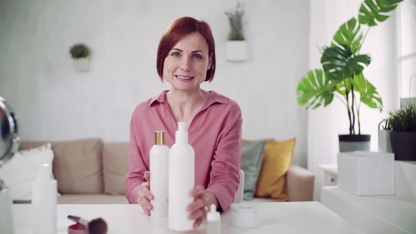 A front view of young woman vlogger indoors, making video about beauty products. Slow motion.