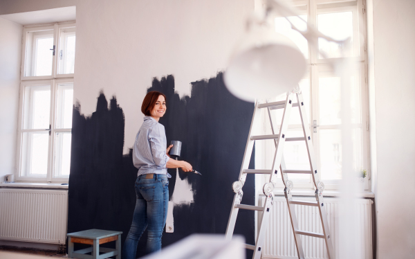 A portrait of young creative woman painting wall black. A startup of small business.