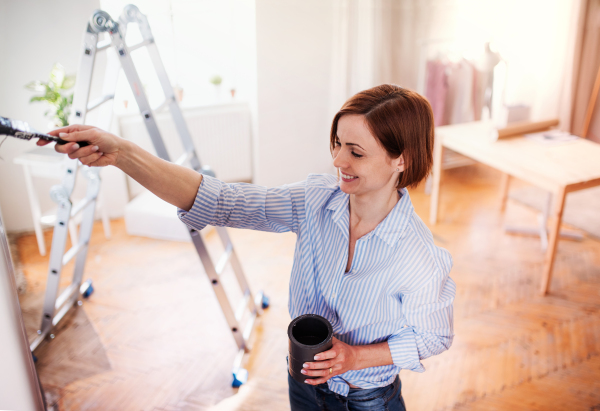 A portrait of young creative woman painting wall black. A startup of small business.