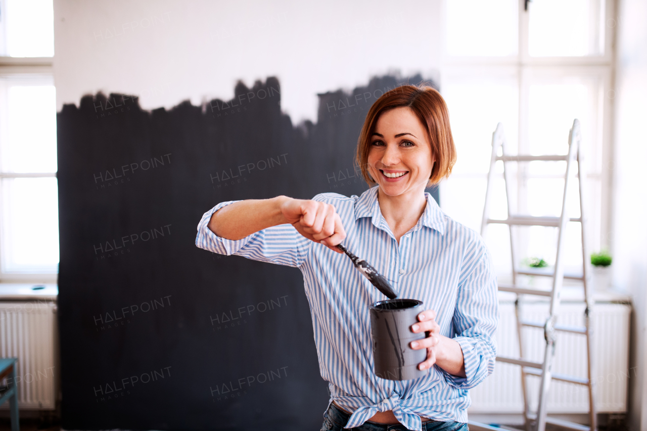 A portrait of young creative woman painting wall black. A startup of small business.