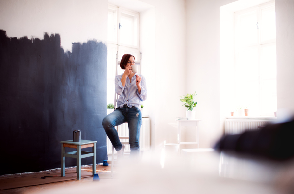 A portrait of young creative woman with a cup of coffee painting wall black. A startup of small business.