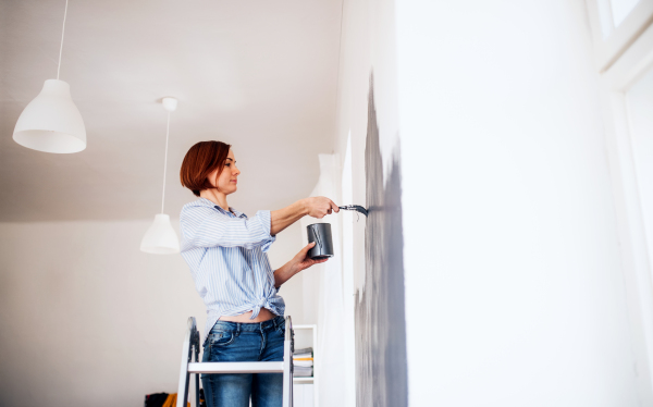 A portrait of young creative woman painting wall black. A startup of small business.