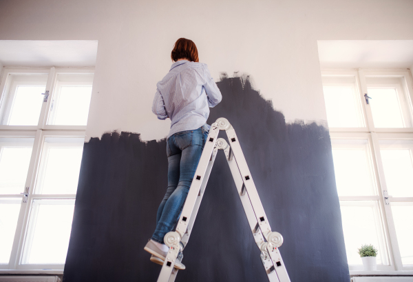 A rear view of young creative woman painting wall black. A startup of small business.