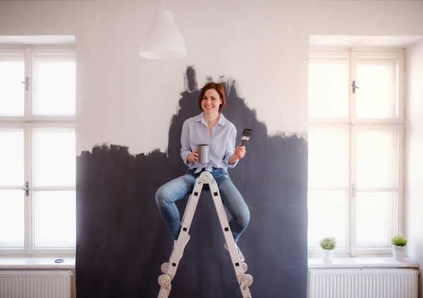 A portrait of young creative woman painting wall black. A startup of small business.