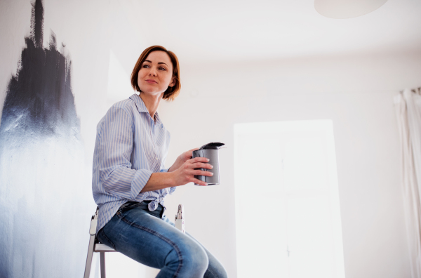 A portrait of young creative woman painting wall black. A startup of small business.