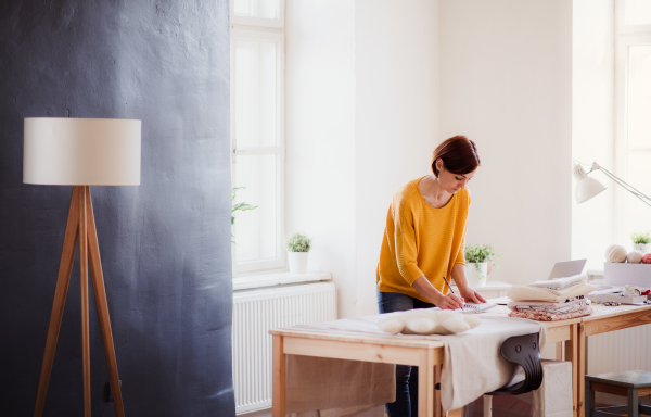 Young creative woman with laptop working in a studio, startup of small tailoring business.