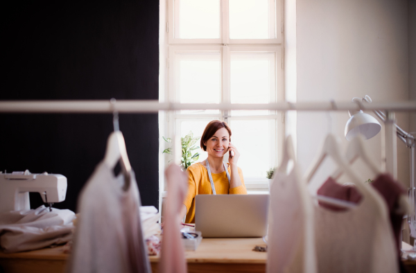 Young creative woman in a studio, using smartphone. A startup of small tailoring business. Copy space.