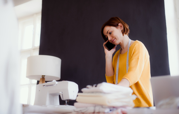 Young creative woman in a studio, using smartphone. A startup of small tailoring business. Copy space.