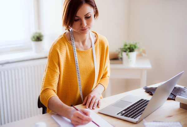 Young creative woman with laptop working in a studio, startup of small tailoring business.