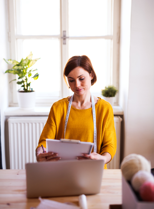 Young creative woman with laptop in a studio. A startup of small tailoring business.