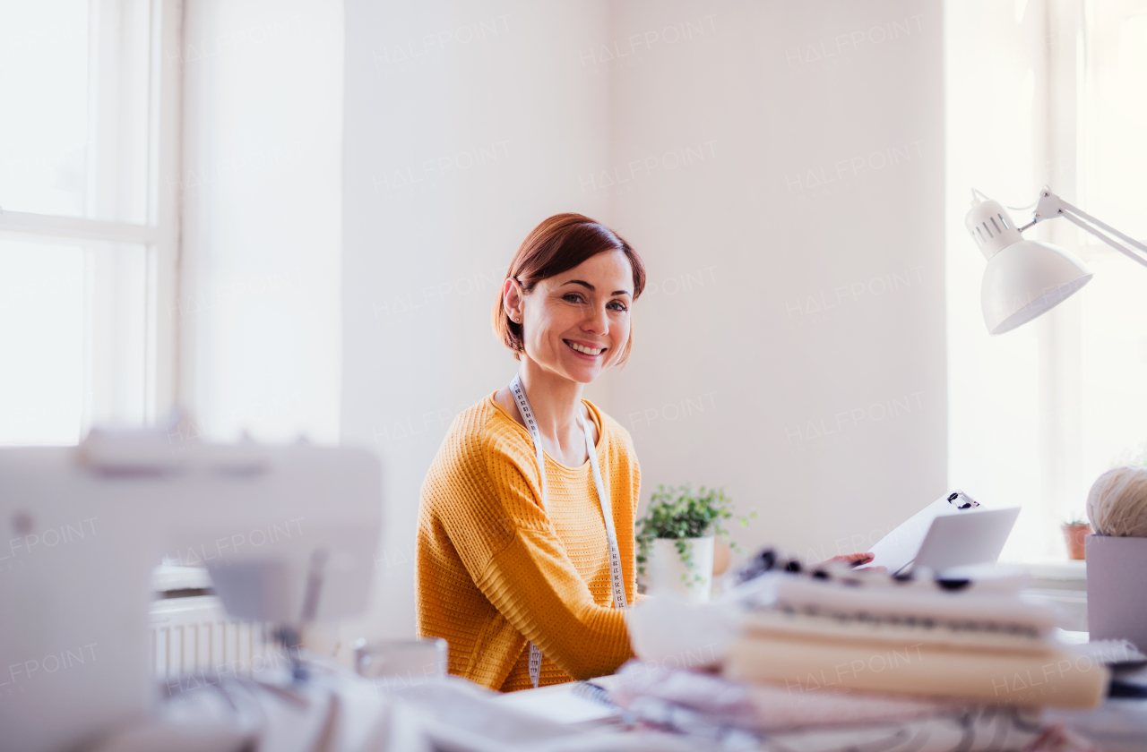 Young creative woman with laptop working in a studio, startup of small tailoring business.