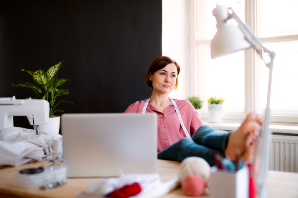 Young creative woman in a studio, resting with feet on desk. A startup of small tailoring business.