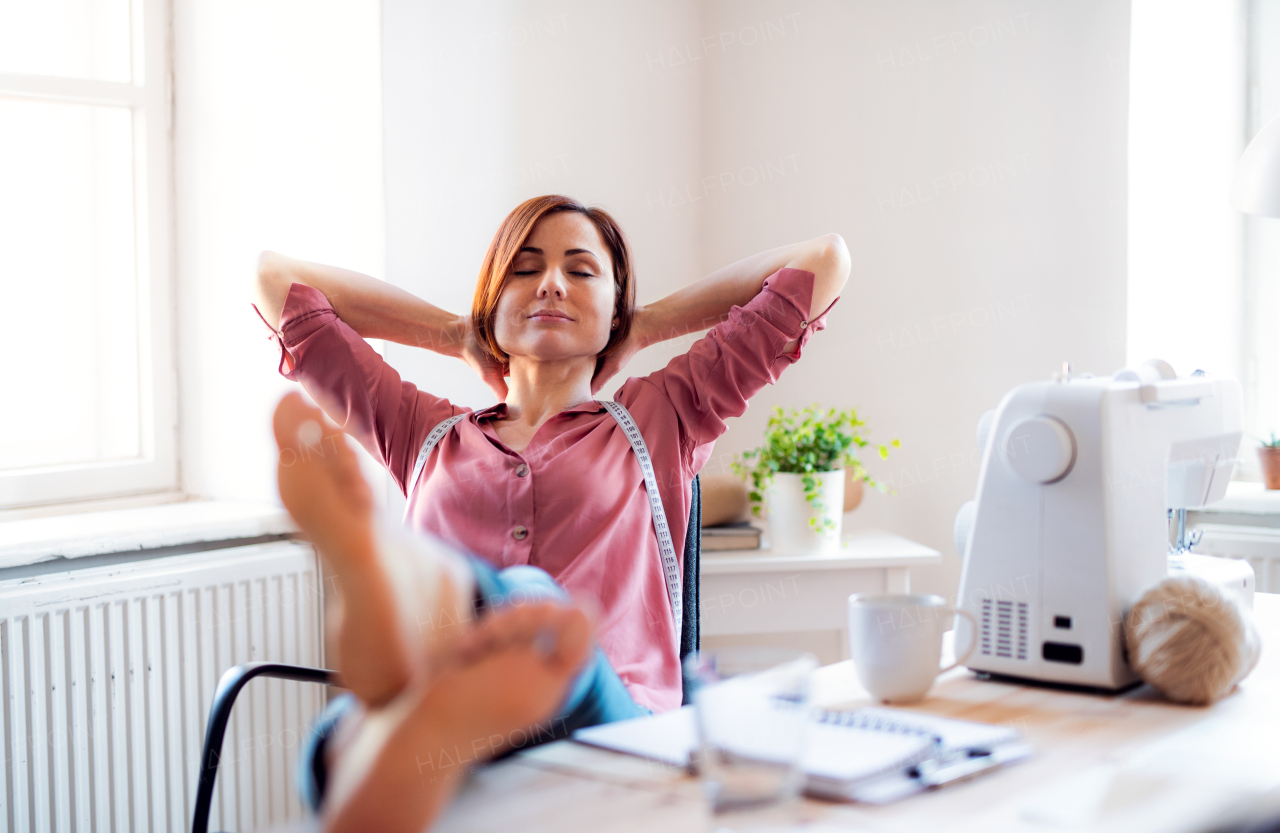 Young creative woman in a studio, resting with feet on desk. A startup of small tailoring business.