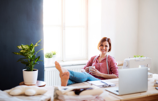 Young creative woman with coffee in a studio, resting with feet on desk. A startup of small tailoring business.