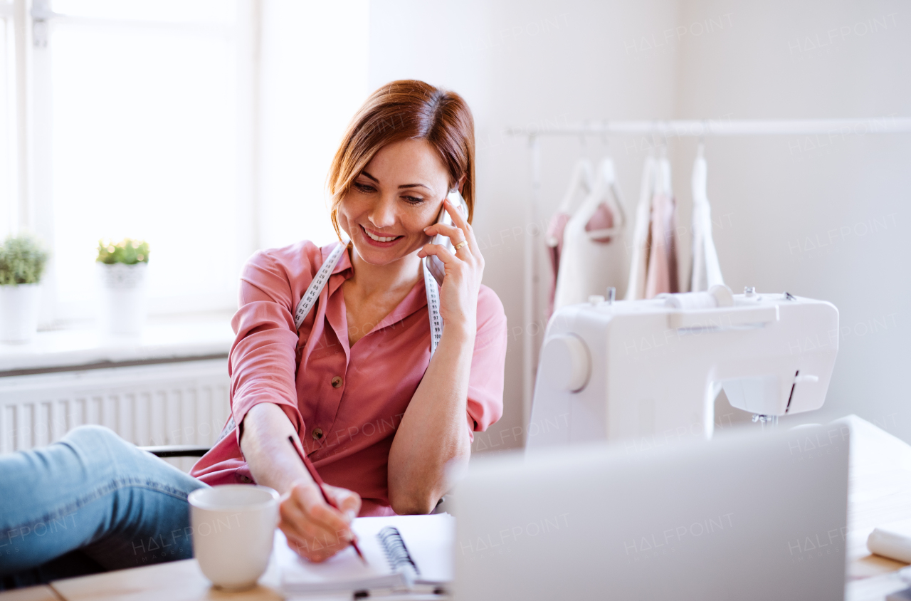 Young creative woman in a studio, using smartphone. A startup of small tailoring business. Copy space.