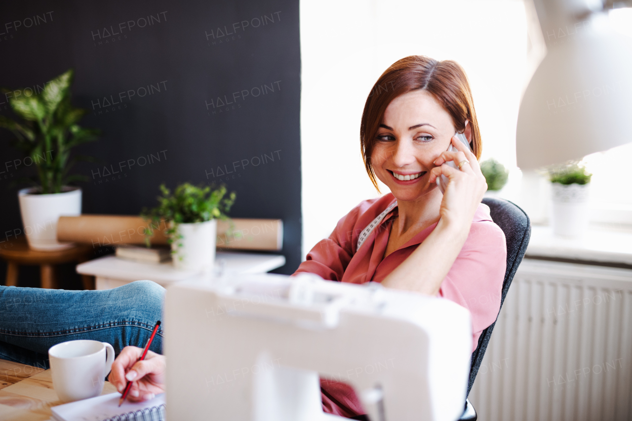 Young creative woman in a studio, using smartphone. A startup of small tailoring business. Copy space.