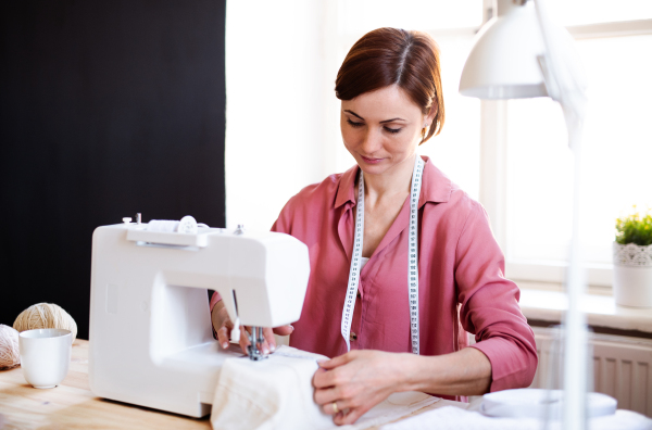 Young creative woman in a studio, working on sewing machine. A startup of small tailoring business.