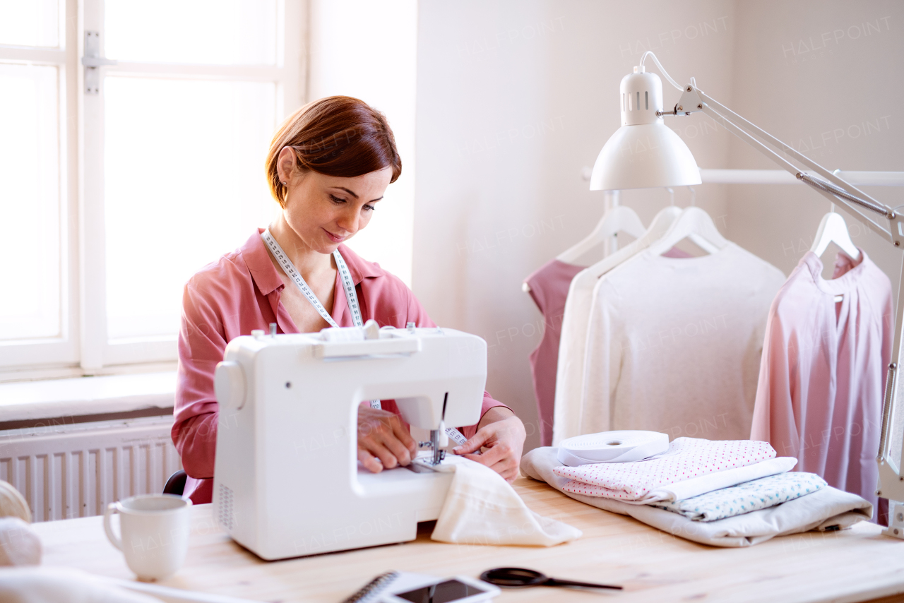 Young creative woman in a studio, working on sewing machine. A startup of small tailoring business.