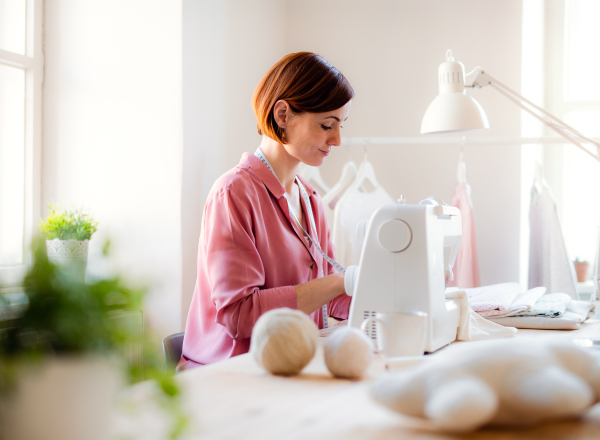 Young creative woman in a studio, working on sewing machine. A startup of small tailoring business.