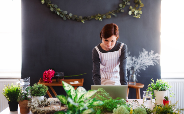 A young creative woman arranging flowers in a flower shop, using laptop. A startup of florist business.