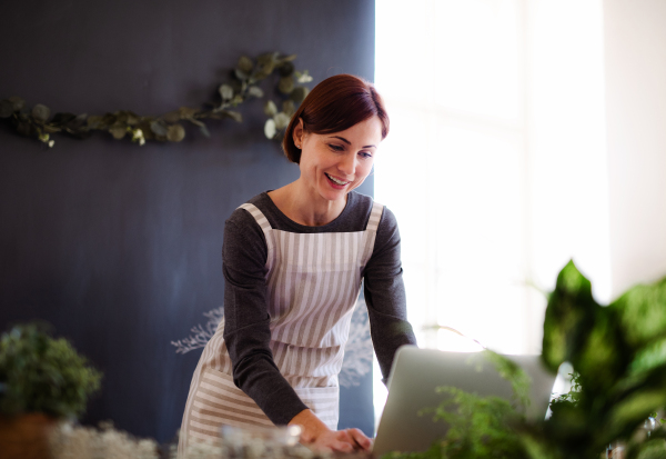 A young creative woman arranging flowers in a flower shop, using laptop. A startup of florist business.