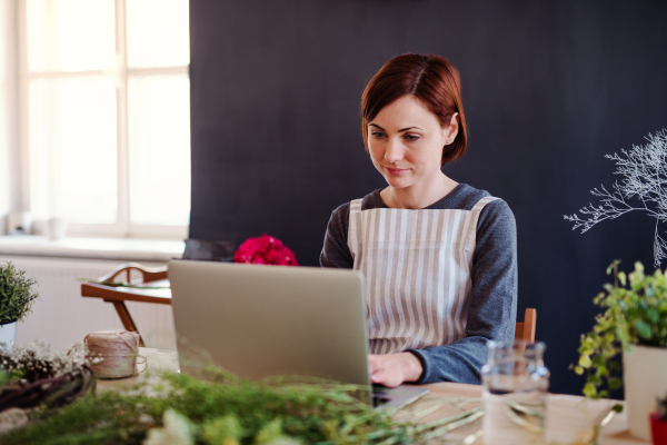 A young creative woman arranging flowers in a flower shop, using laptop. A startup of florist business.