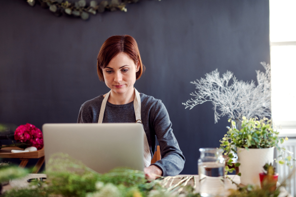 A young creative woman arranging flowers in a flower shop, using laptop. A startup of florist business.