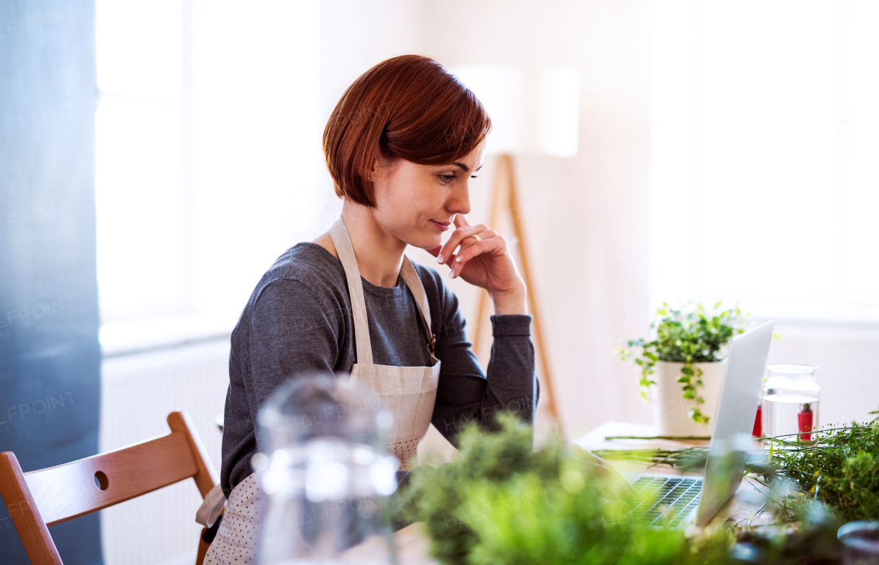 A young creative woman arranging flowers in a flower shop, using laptop. A startup of florist business.