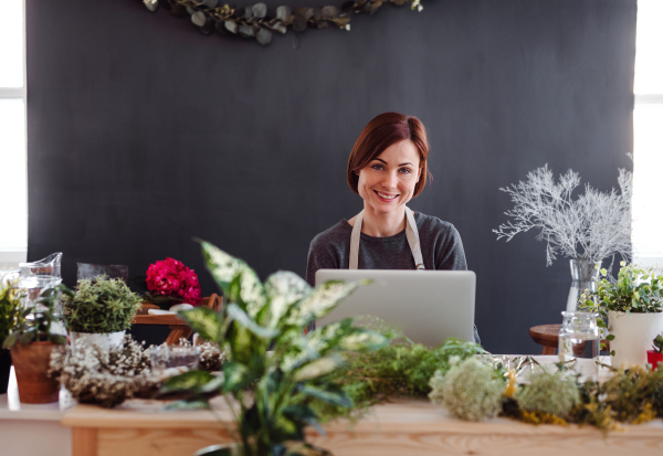 A young creative woman arranging flowers in a flower shop, using laptop. A startup of florist business.